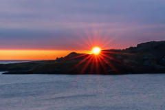 Golden sun setting over rugged cliffs on a Newfoundland whale watching tour.